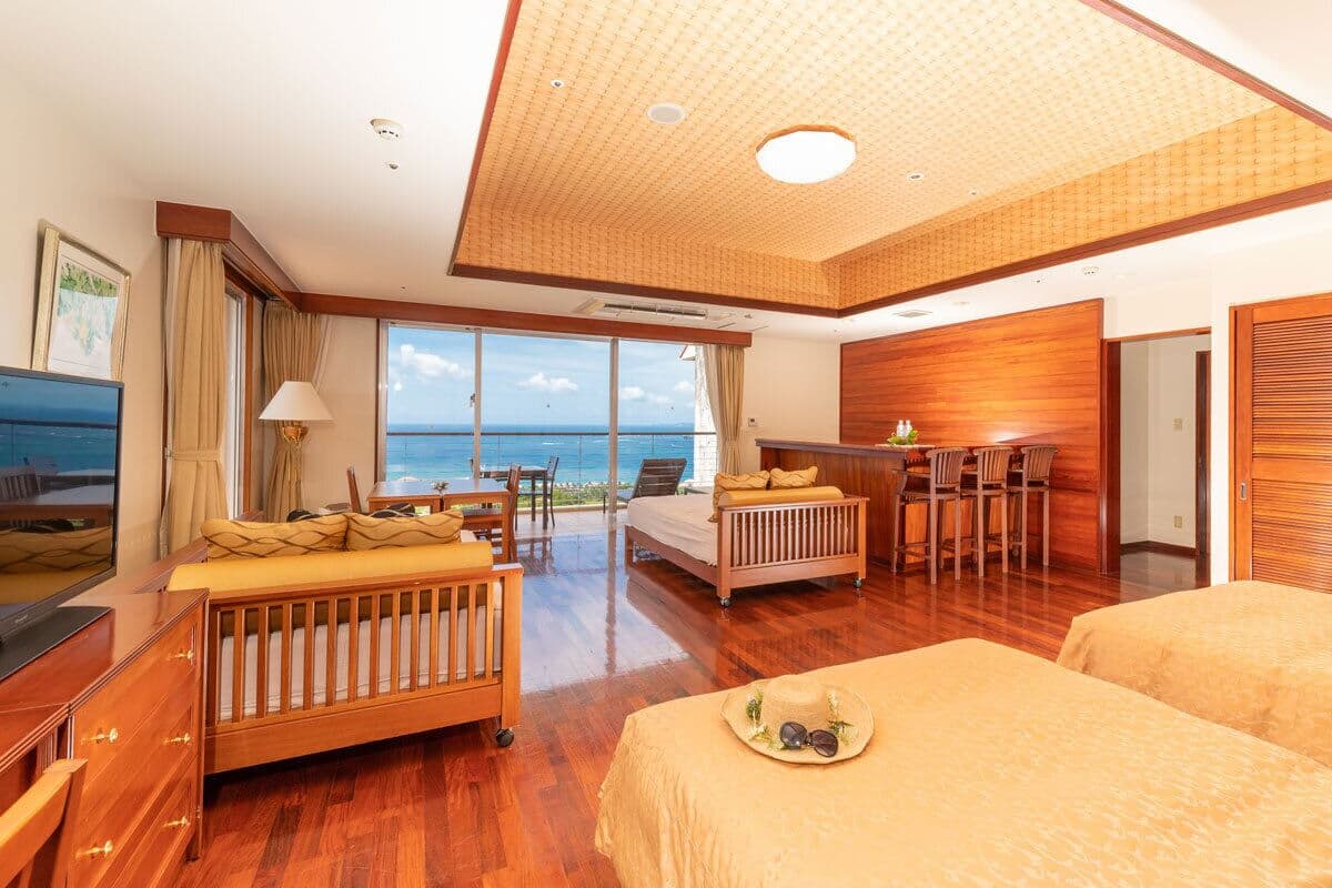 A hotel room with a wooden floor, a bed, a desk, and a view of the ocean.