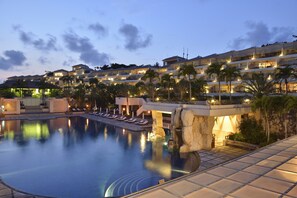 A large swimming pool with lounge chairs, palm trees, and a hotel building in the background.