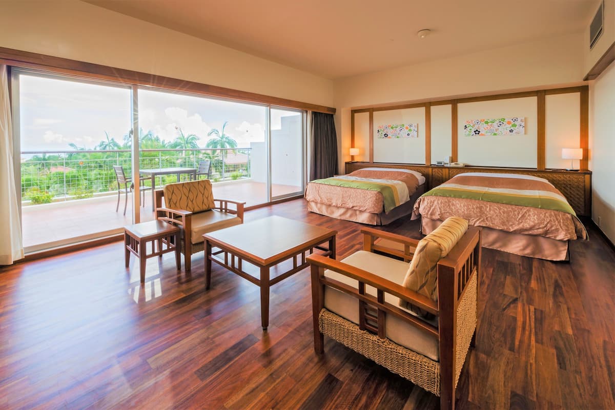 A hotel room with a balcony, two beds, a dining table, and a chair.