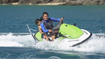 A person riding a green and white Kawasaki jet ski on a body of water with a rocky shoreline in the background.