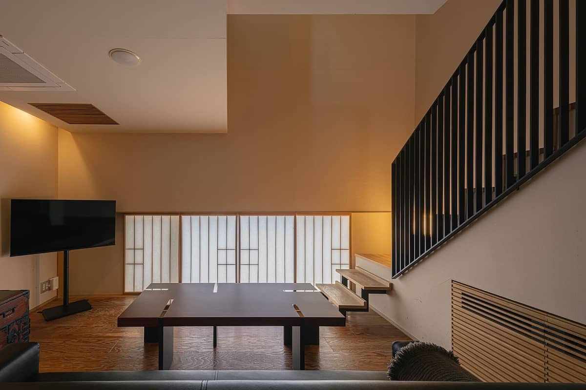 Un interior moderno con una televisión de pantalla plana, una mesa de madera y una escalera con barandillas negras.