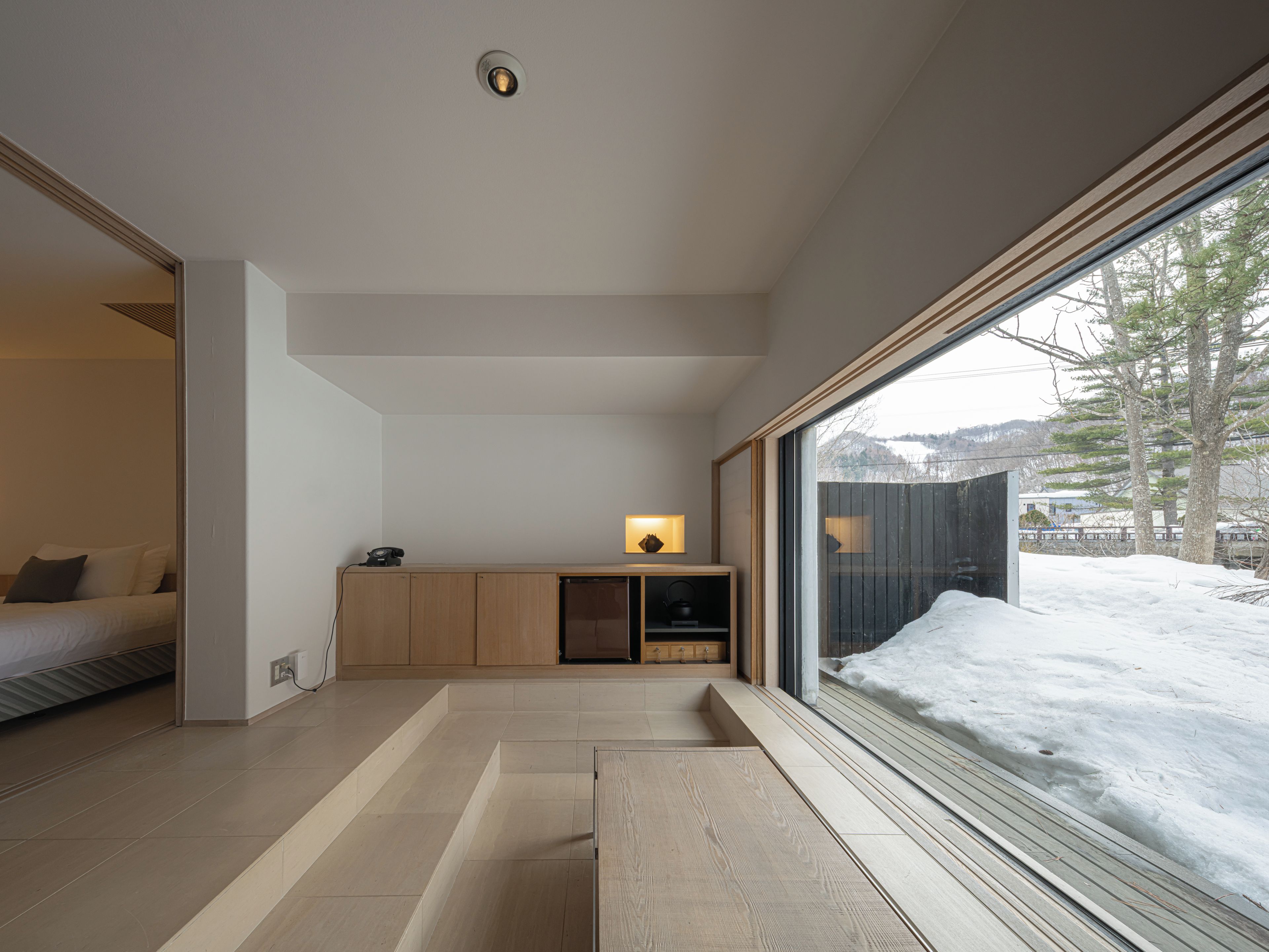 A modern interior with a wooden bench, a small table, and a window overlooking a snowy landscape.