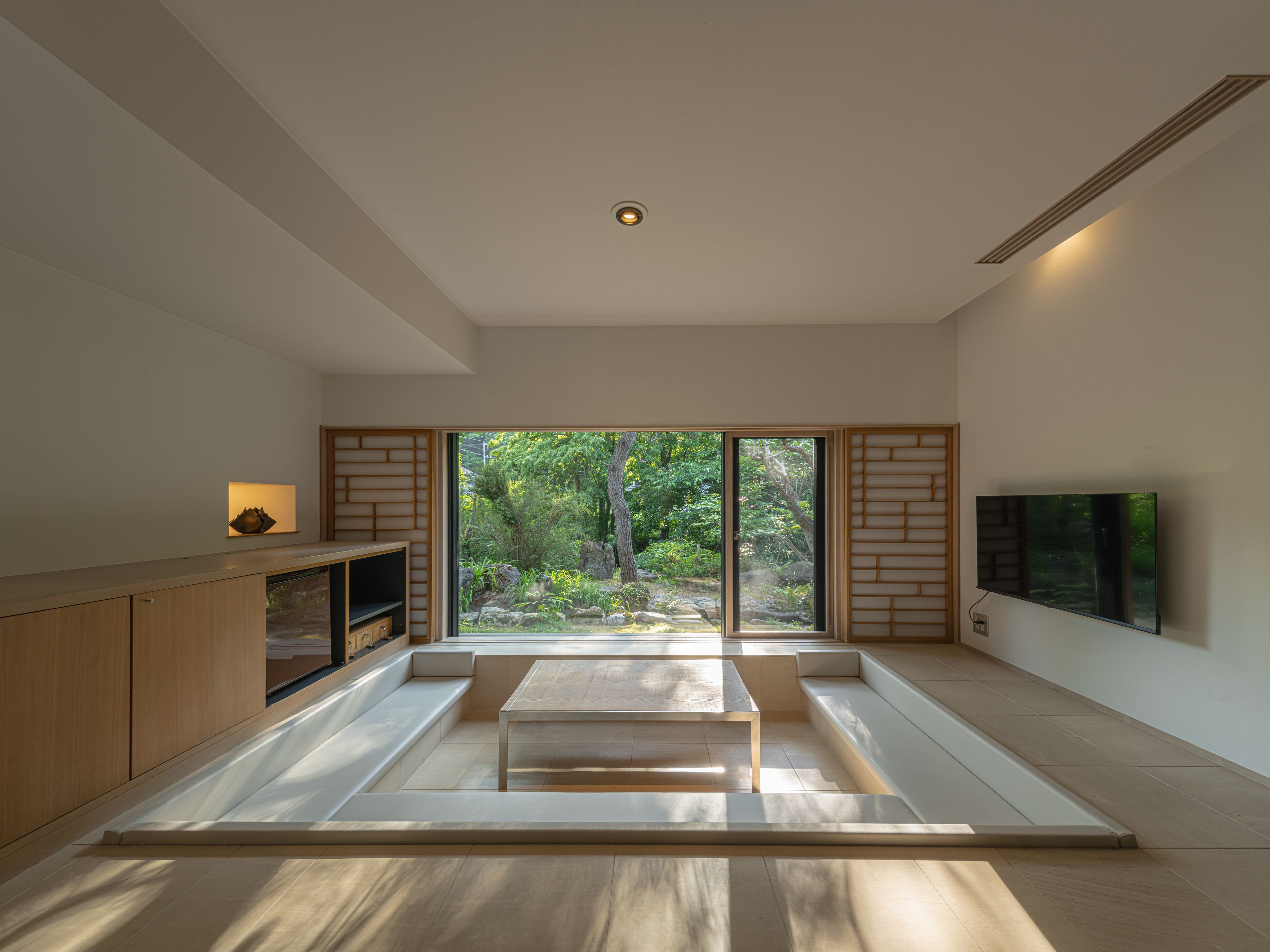 A modern interior with a sliding glass door leading to a garden, a flat-screen TV mounted on the wall, and a wooden cabinet.