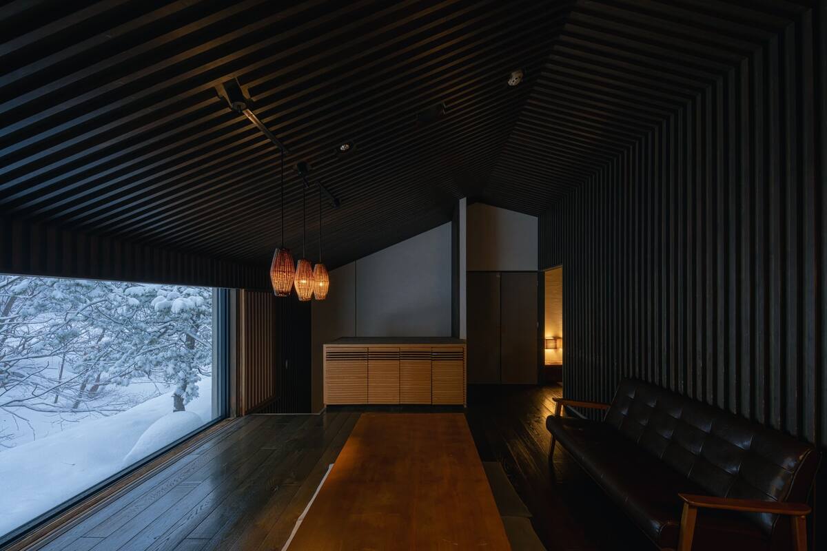 Un interior moderno con suelo de madera, techo oscuro y un amplio ventanal con vistas a un paisaje nevado.