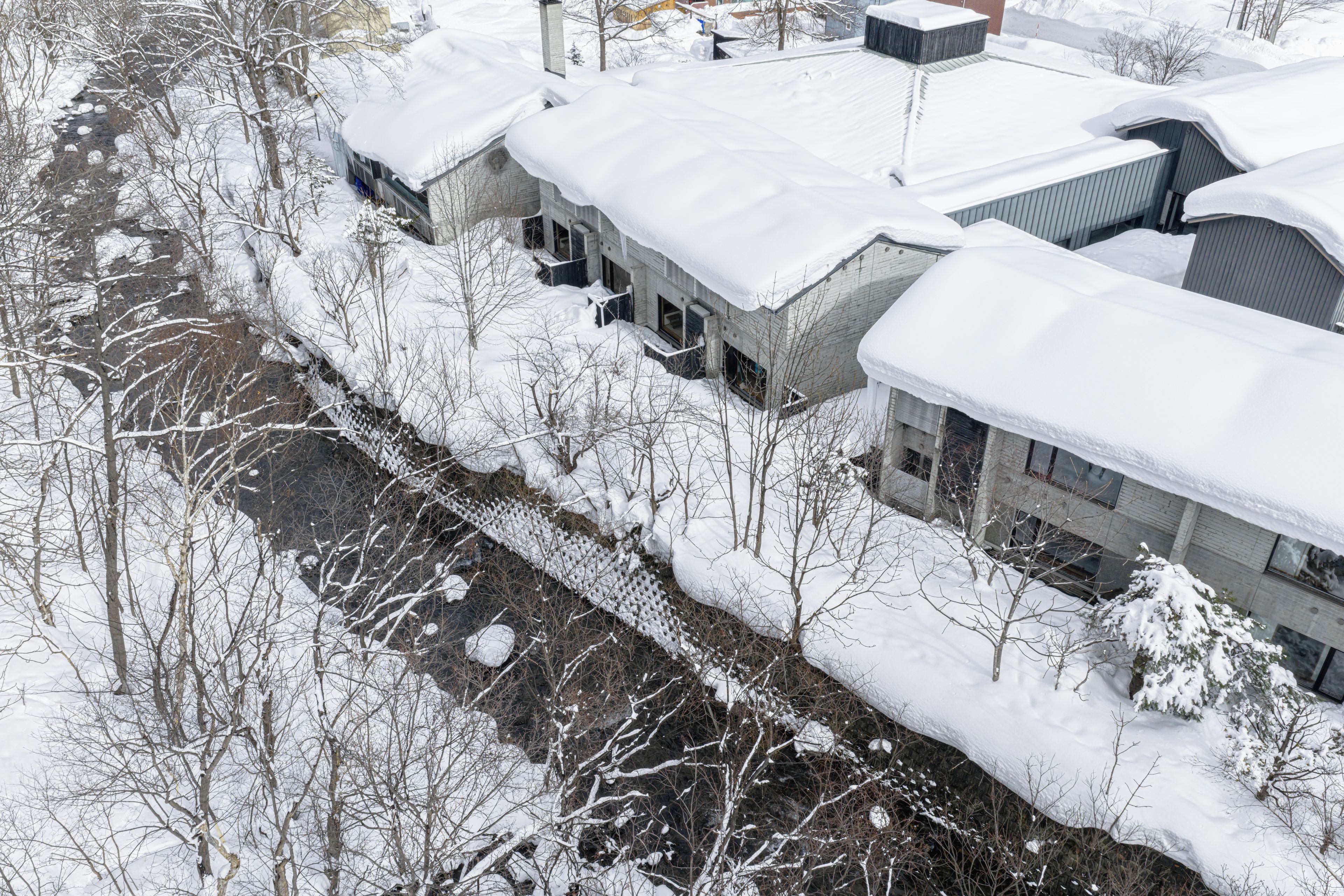 A snow-covered building with multiple windows and a river in the foreground.