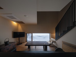 A modern living room with a large window, a flat-screen TV, a wooden table, and a staircase. - OTARU RETREAT KURAMURE by Onko Chishin (Otaru)
