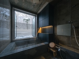 A modern bathroom with a large window, a built-in shower, and a wooden stool.