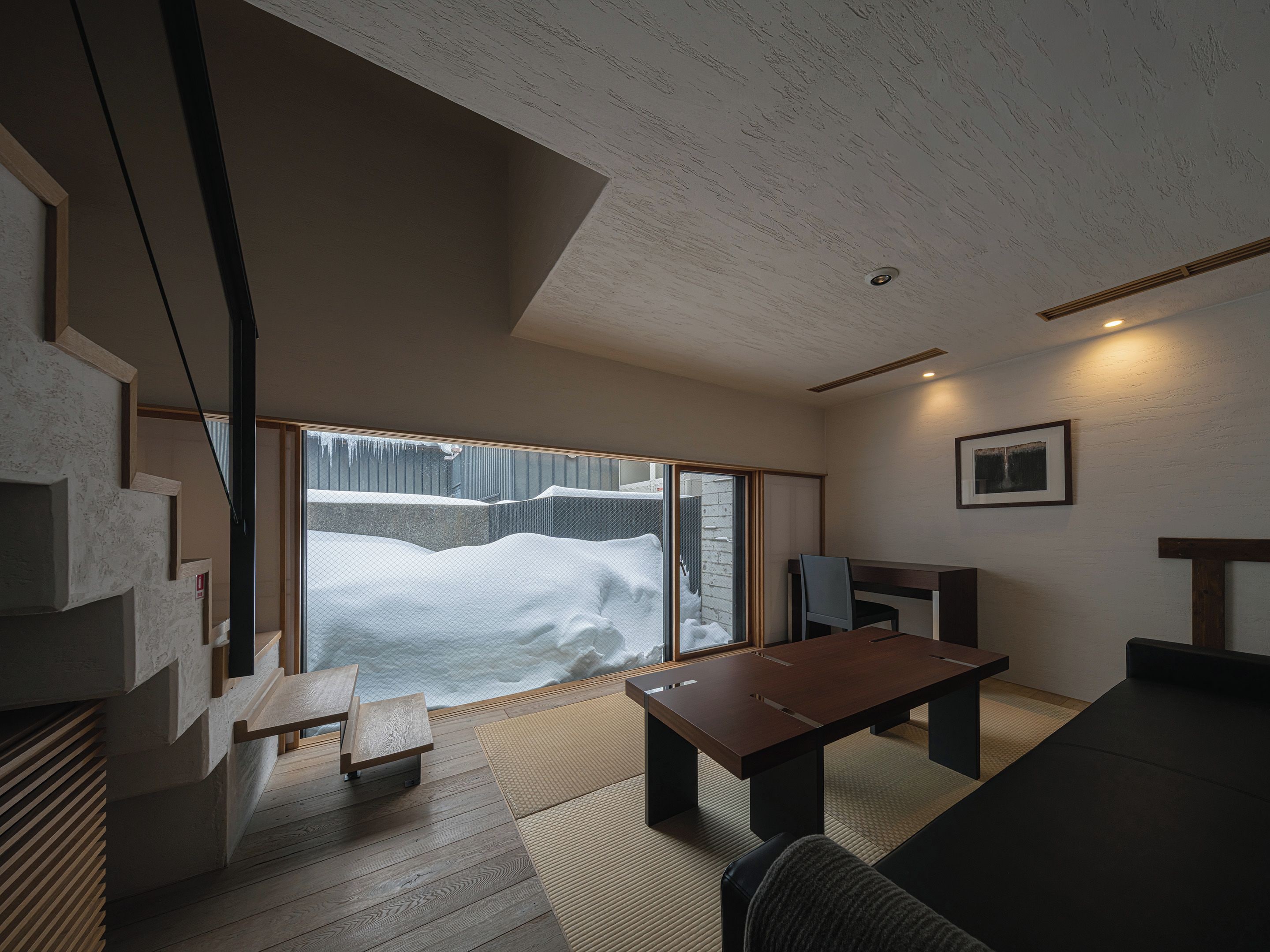 A modern interior with a wooden floor, a large window with a view of snow-covered trees, a wooden table, and a sofa.