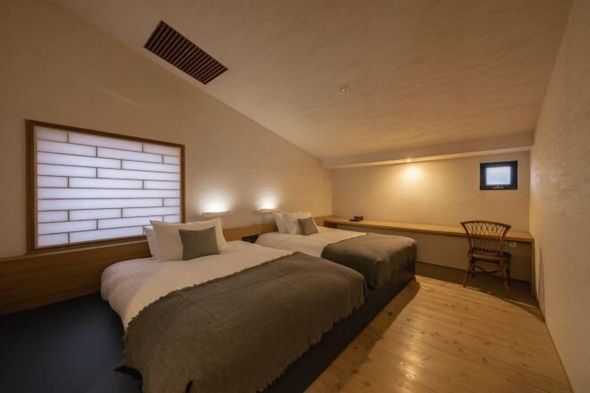 Un dormitorio con dos camas, un escritorio, una silla y una ventana con persianas.