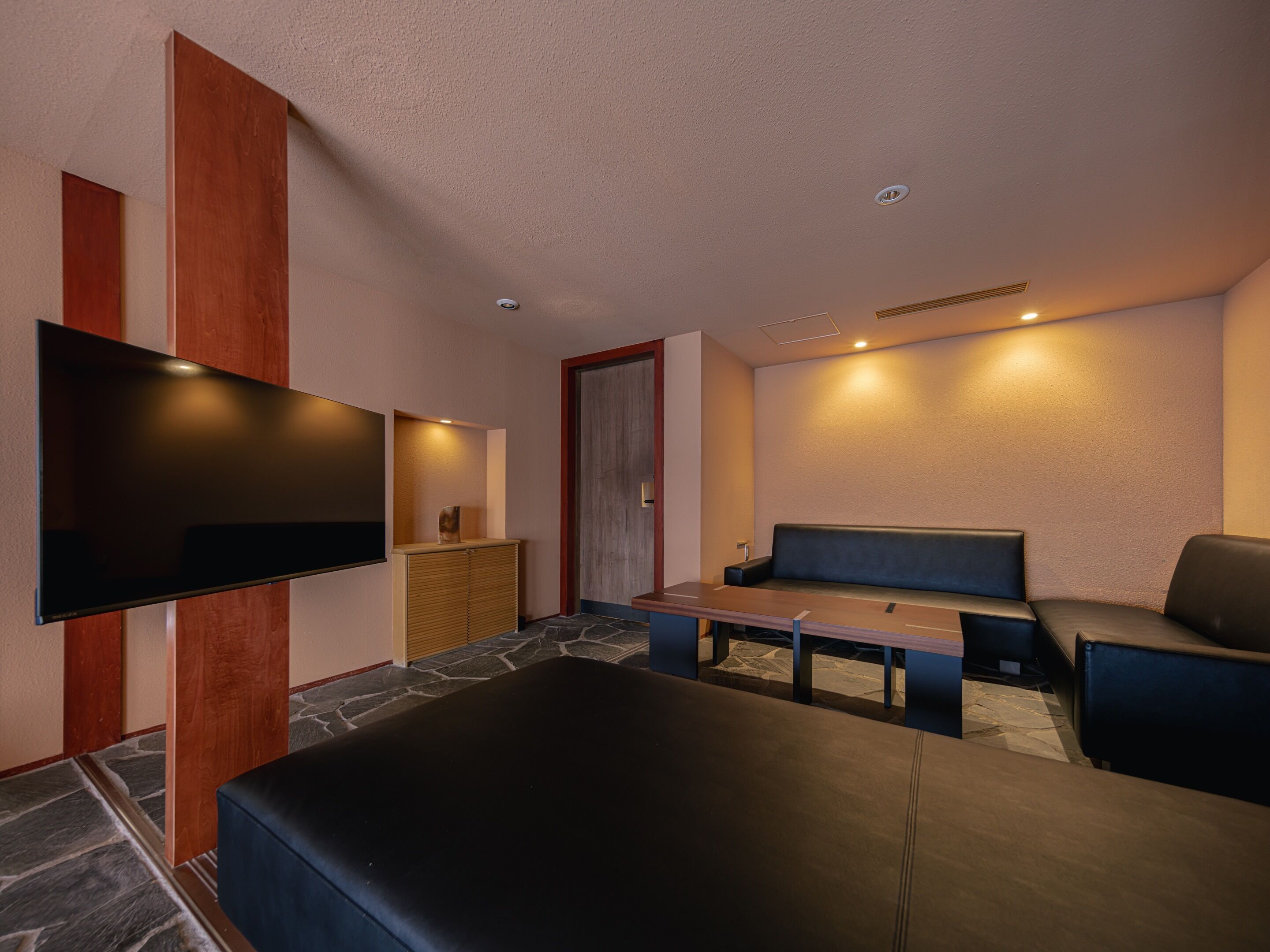 A modern living room with a flat-screen TV, a sofa, a coffee table, and a stone-patterned floor.