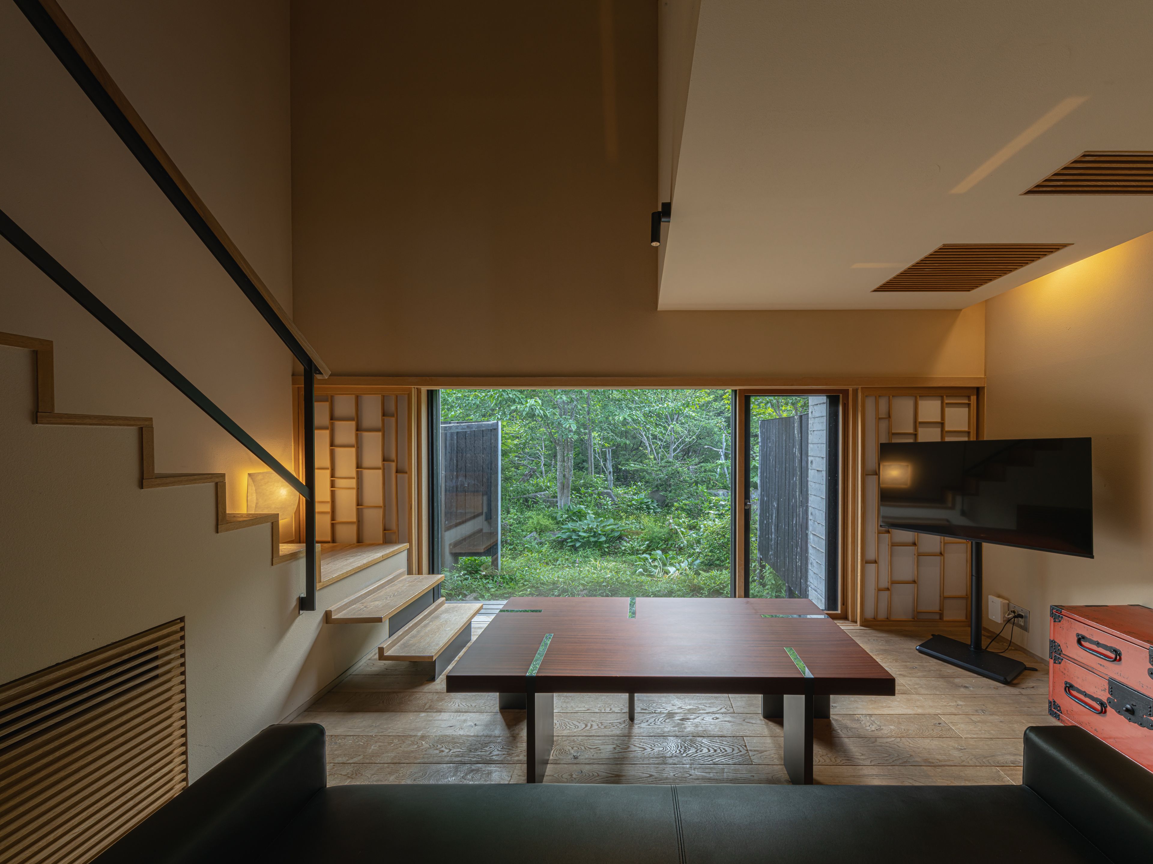 Un interior moderno con una escalera de madera, una mesa grande y un televisor.