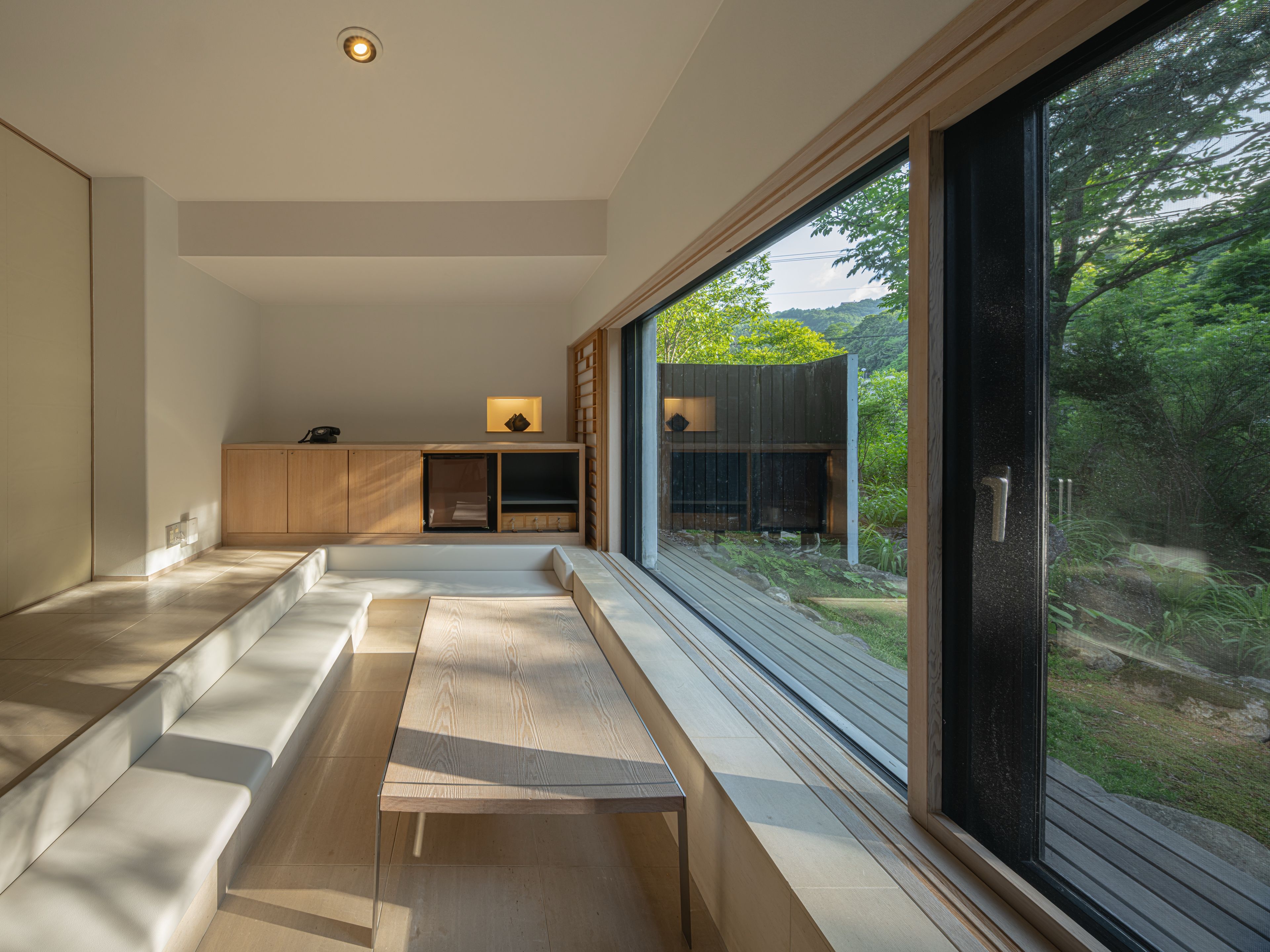 Un interior moderno con un banco incorporado, un armario de madera y un ventanal con vistas a la vegetación.