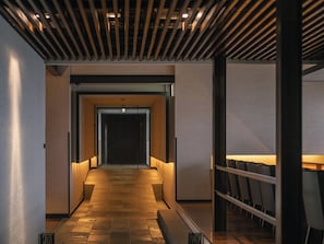 A corridor with a wooden slatted ceiling, a tiled floor, and a seating area with tables and chairs. - OTARU RETREAT by Onko Chishin (Otaru)