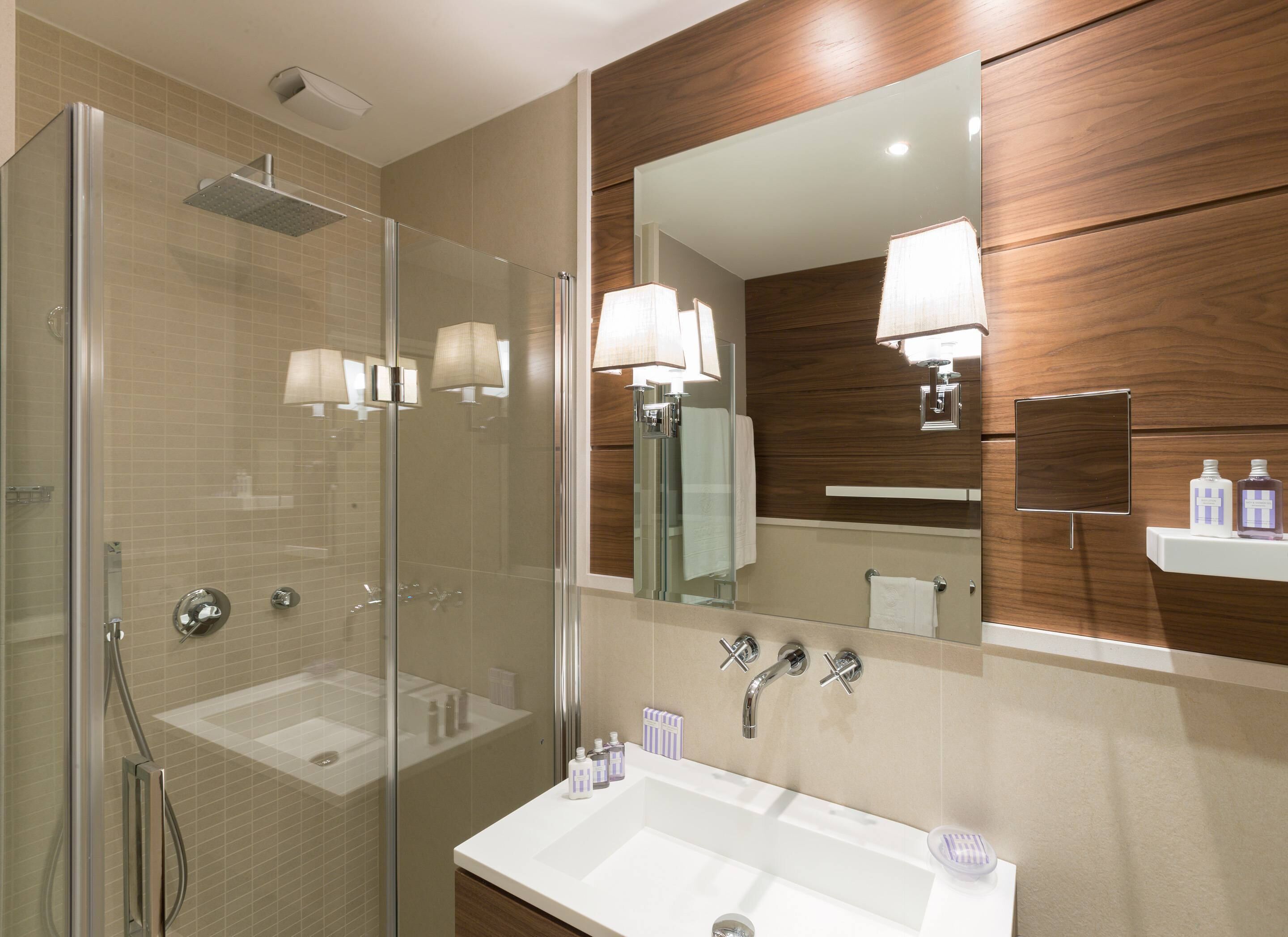 Un bagno moderno con doccia vetro, lavabo con specchio e mobile contenitore in legno.