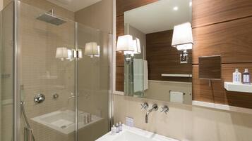 Un bagno moderno con doccia vetro, lavabo con specchio e mobile contenitore in legno.
