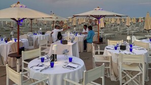 Un espacio exterior para comer con mesas y sillas redondas, un candelabro y sombrillas.