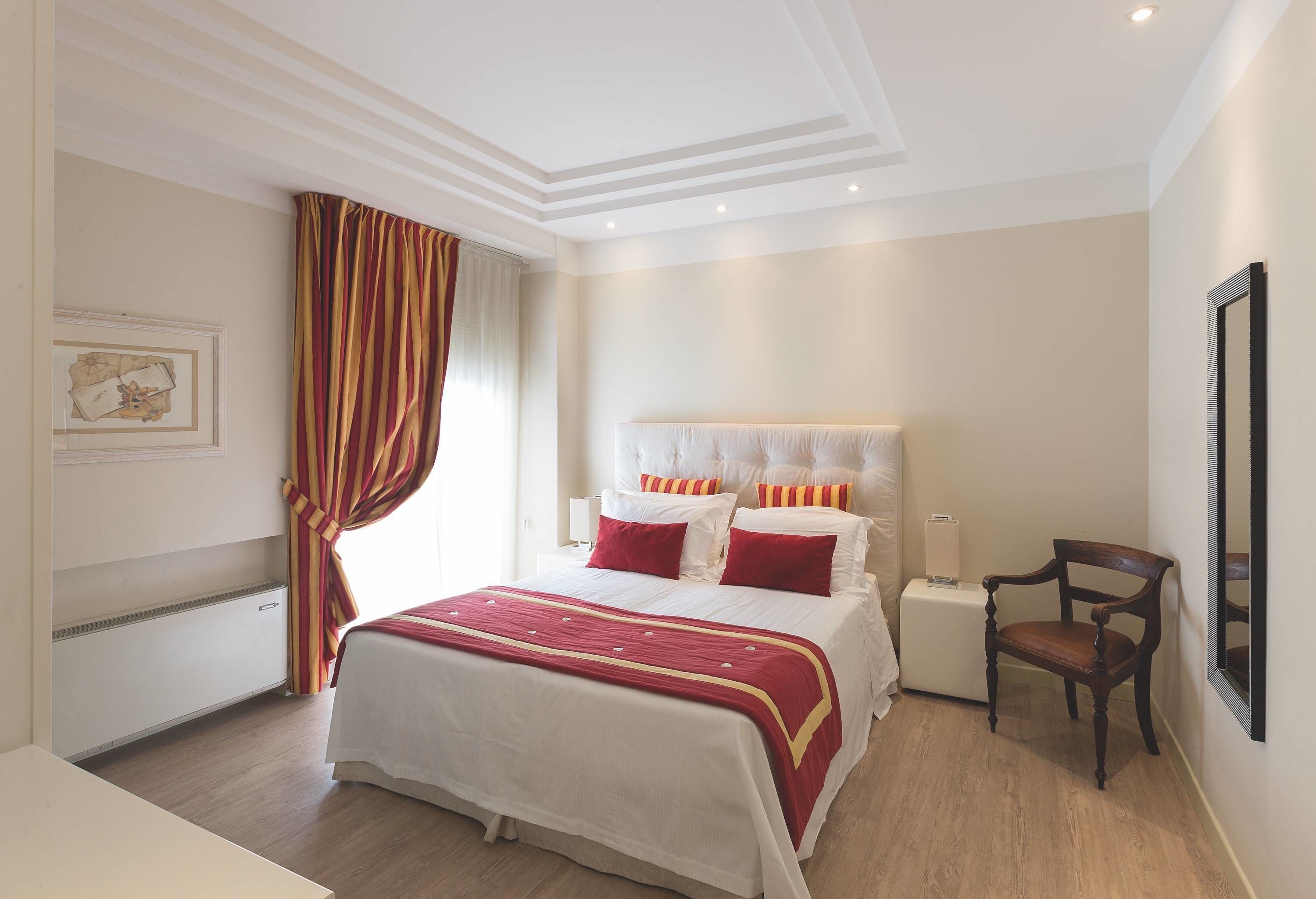 A hotel room with a large bed, a wooden chair, a bedside table, and a framed picture on the wall.