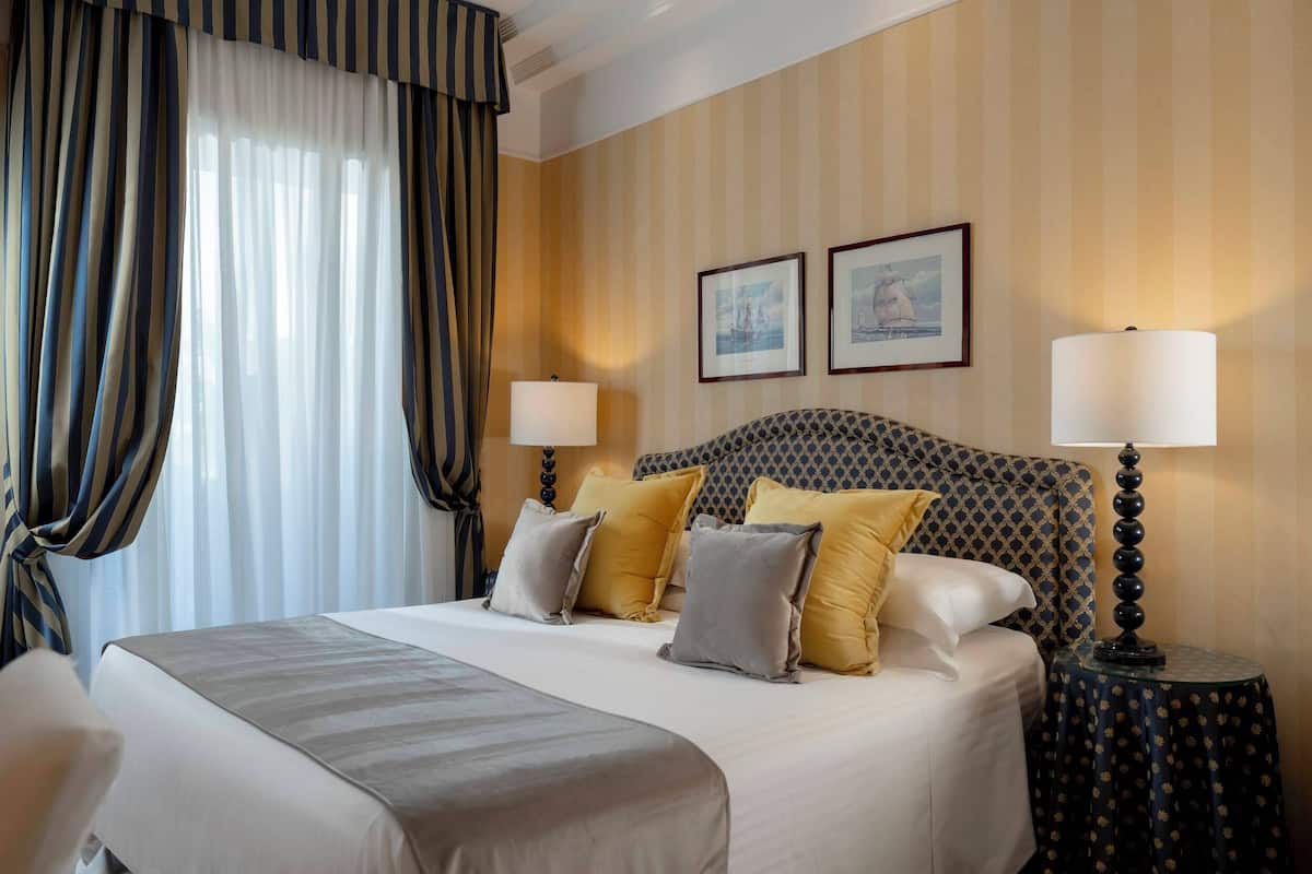 A hotel room with a large bed, two bedside lamps, striped curtains, and two framed pictures on the wall.