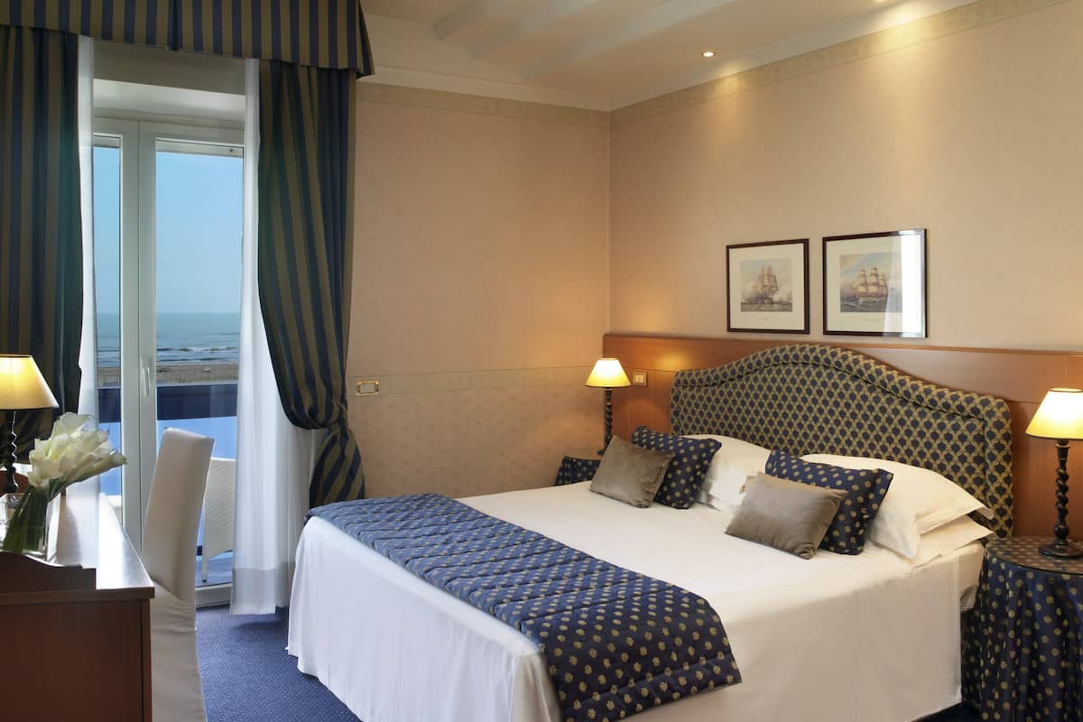 A hotel room with a large bed, two bedside lamps, a headboard with a geometric pattern, and two framed pictures on the wall.