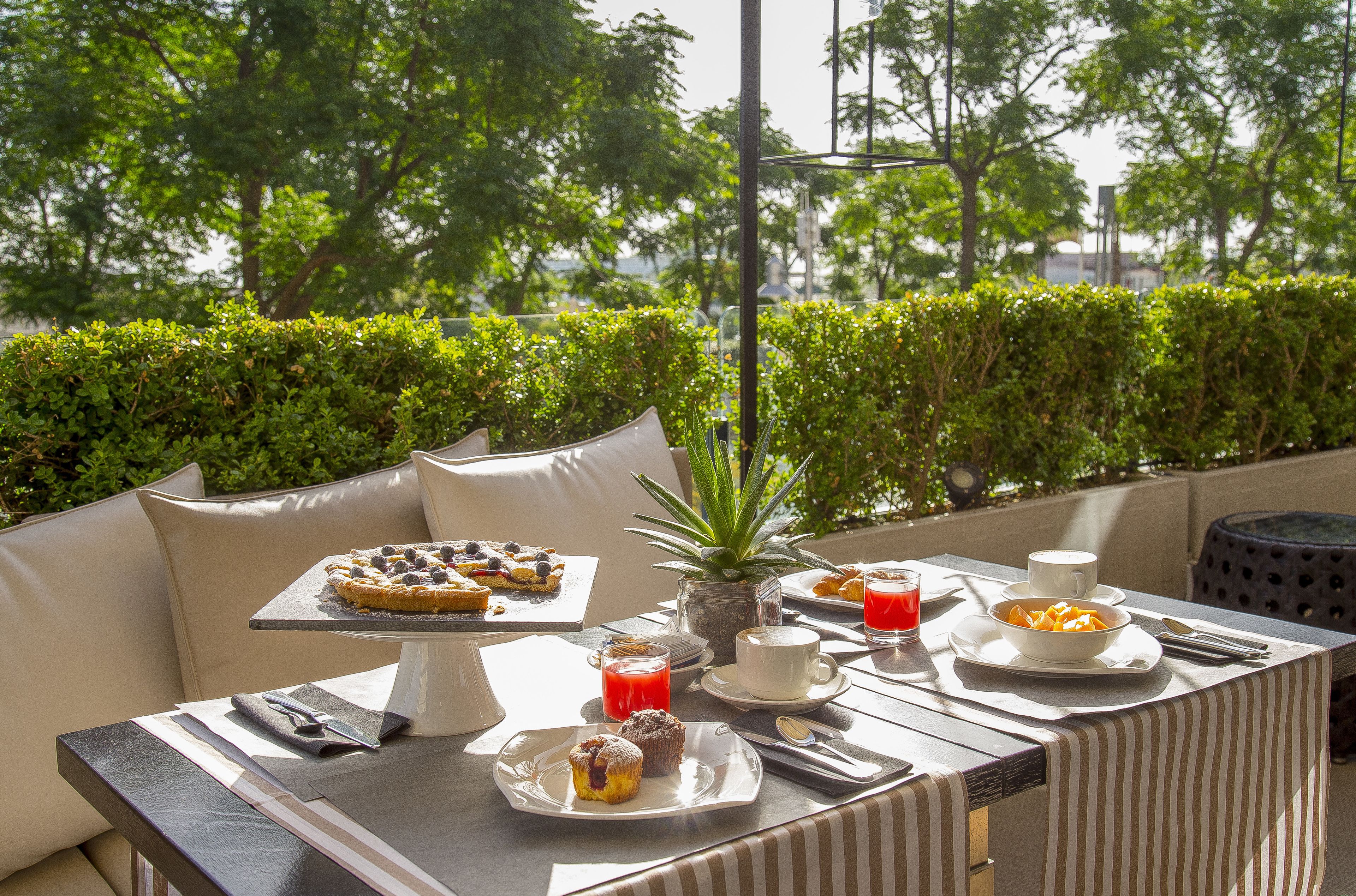 Un área de comedor al aire libre con una mesa dispuesta para el desayuno, incluyendo pasteles, un bol de fruta y bebidas.