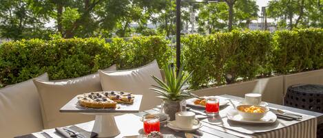 Un área de comedor al aire libre con una mesa dispuesta para el desayuno, incluyendo pasteles, un bol de fruta y bebidas.