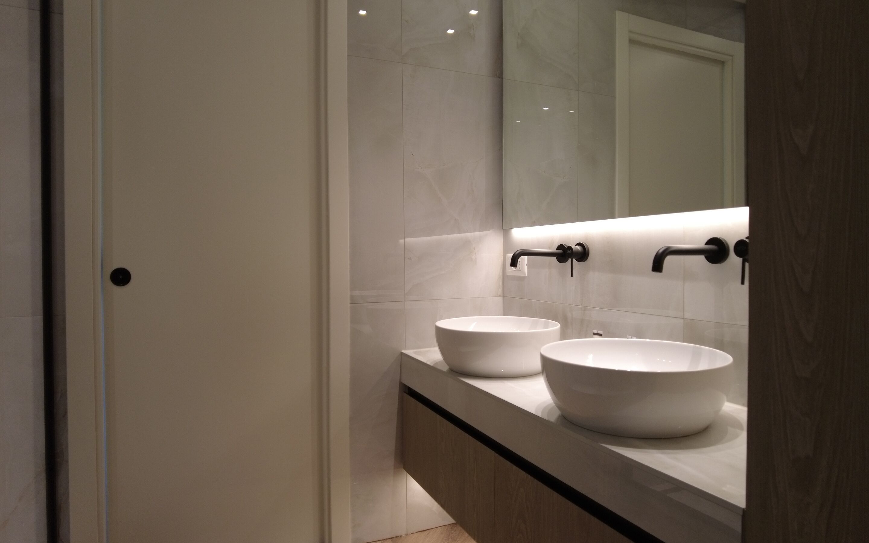 A modern bathroom with two white sinks, a mirror, and a wooden cabinet.