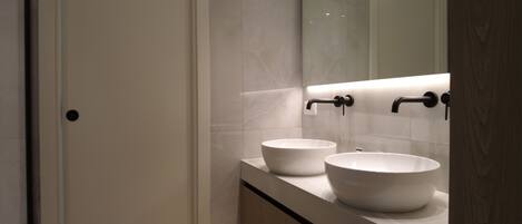 A modern bathroom with two white sinks, a mirror, and a wooden cabinet.