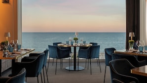 Comedor con una mesa dispuesta para cuatro personas, frente a un ventanal con vista al mar.