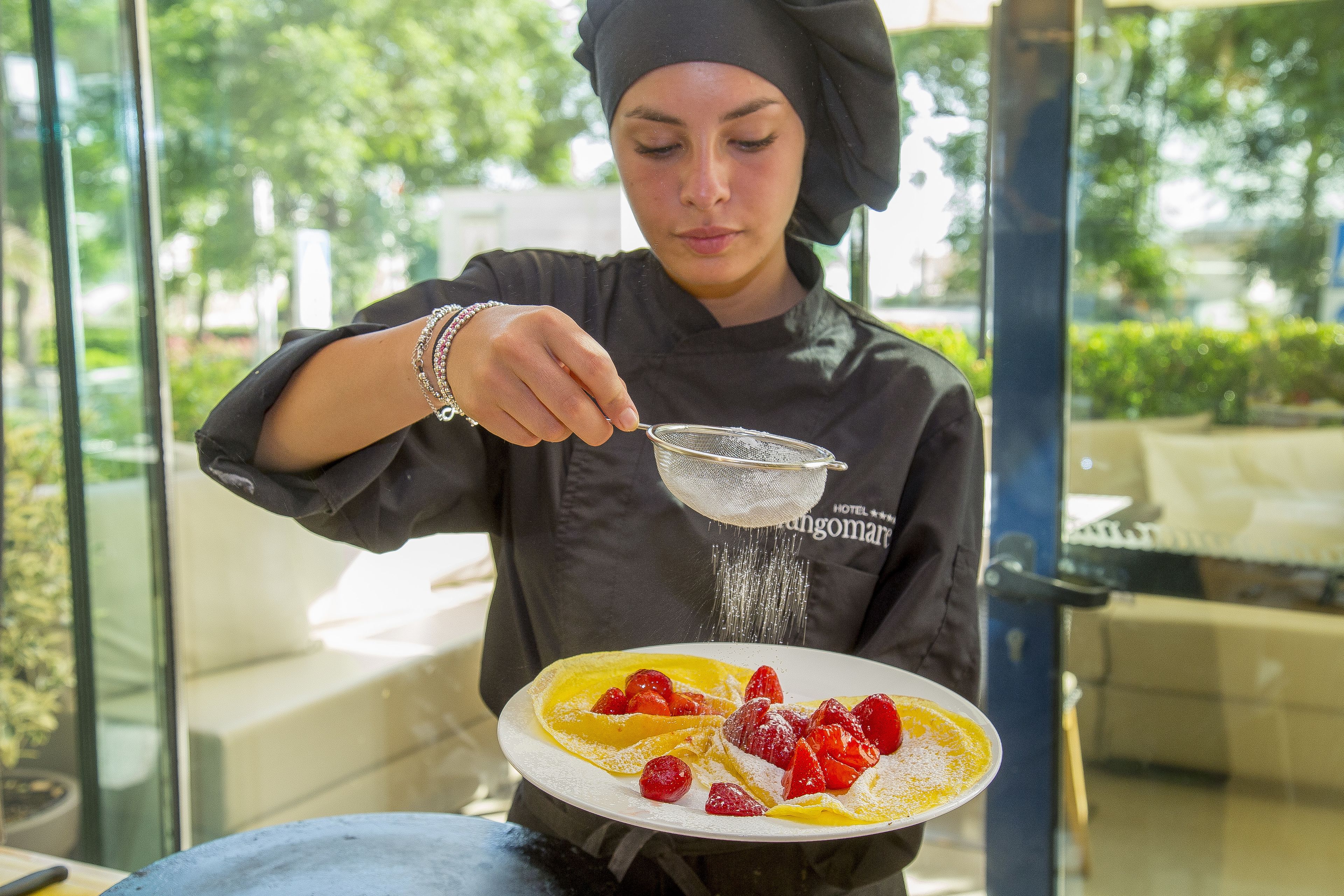 A person in chef attire preparing a dish with strawberries and a strainer.
