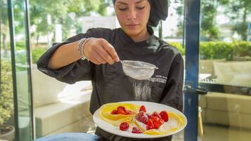 A person in chef attire preparing a dish with strawberries and a strainer.