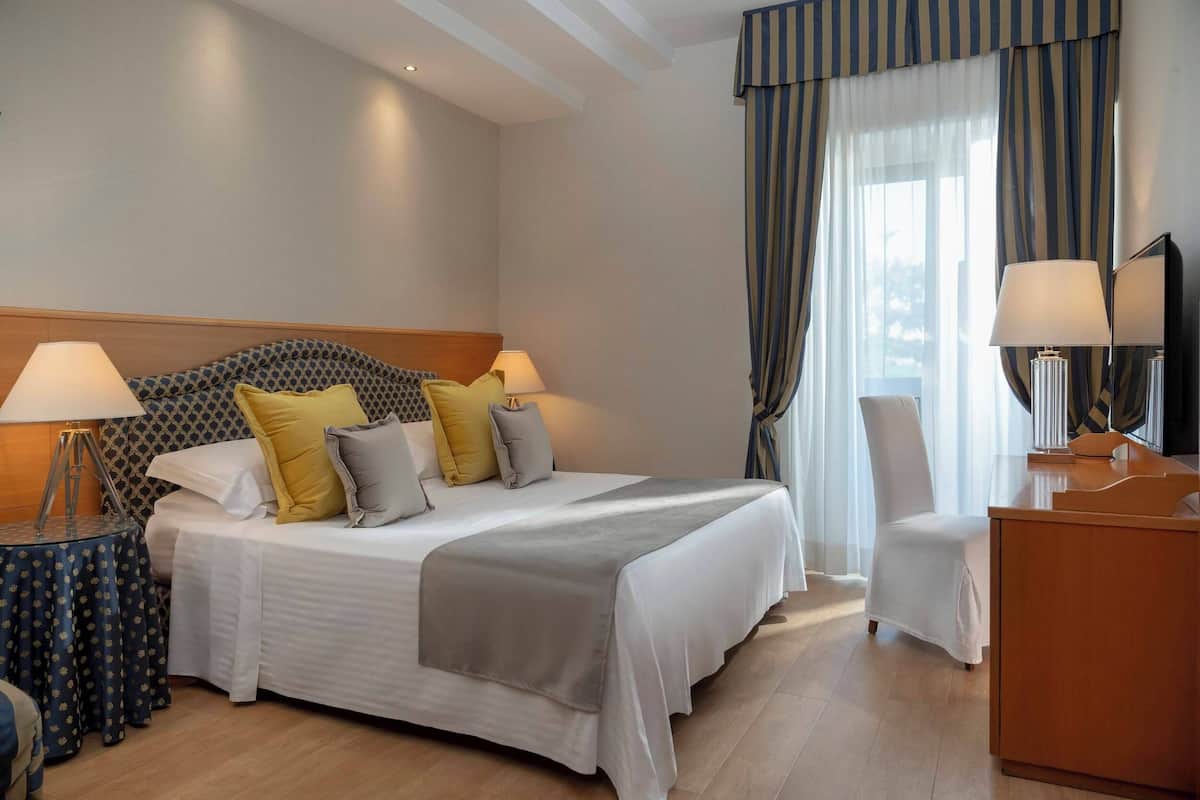 A hotel room with a large bed, two bedside lamps, a desk with a mirror, and a chair.