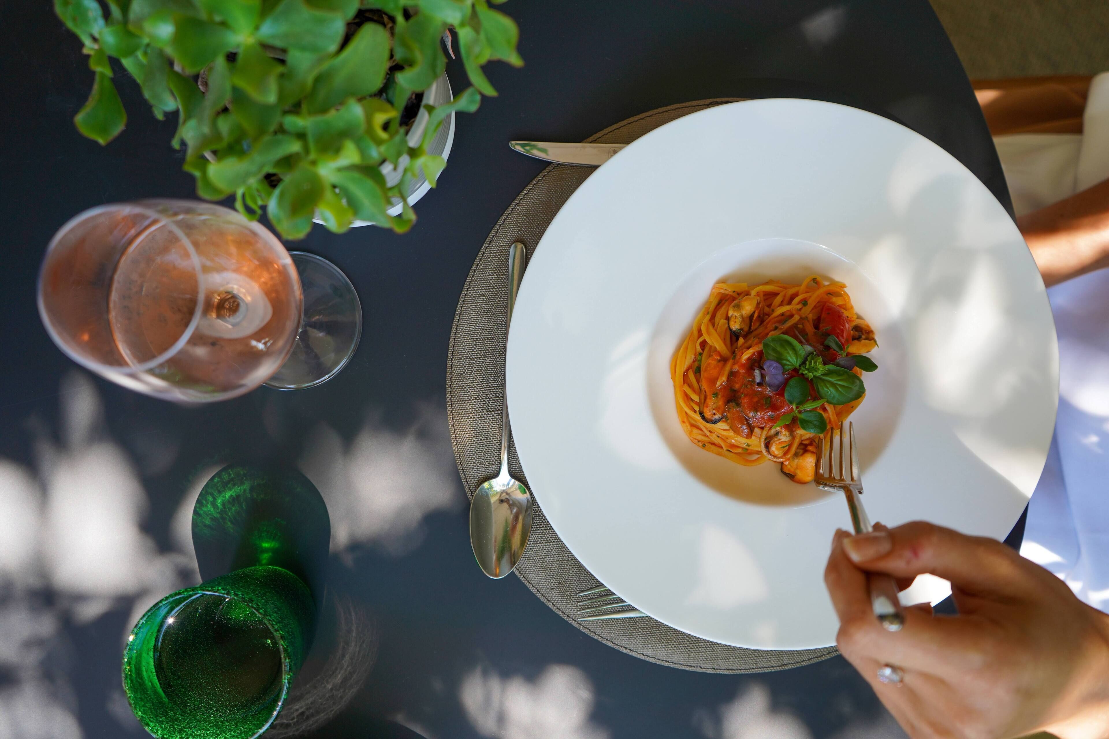 A dining table with a plate of pasta, a glass of wine, and a green glass.
