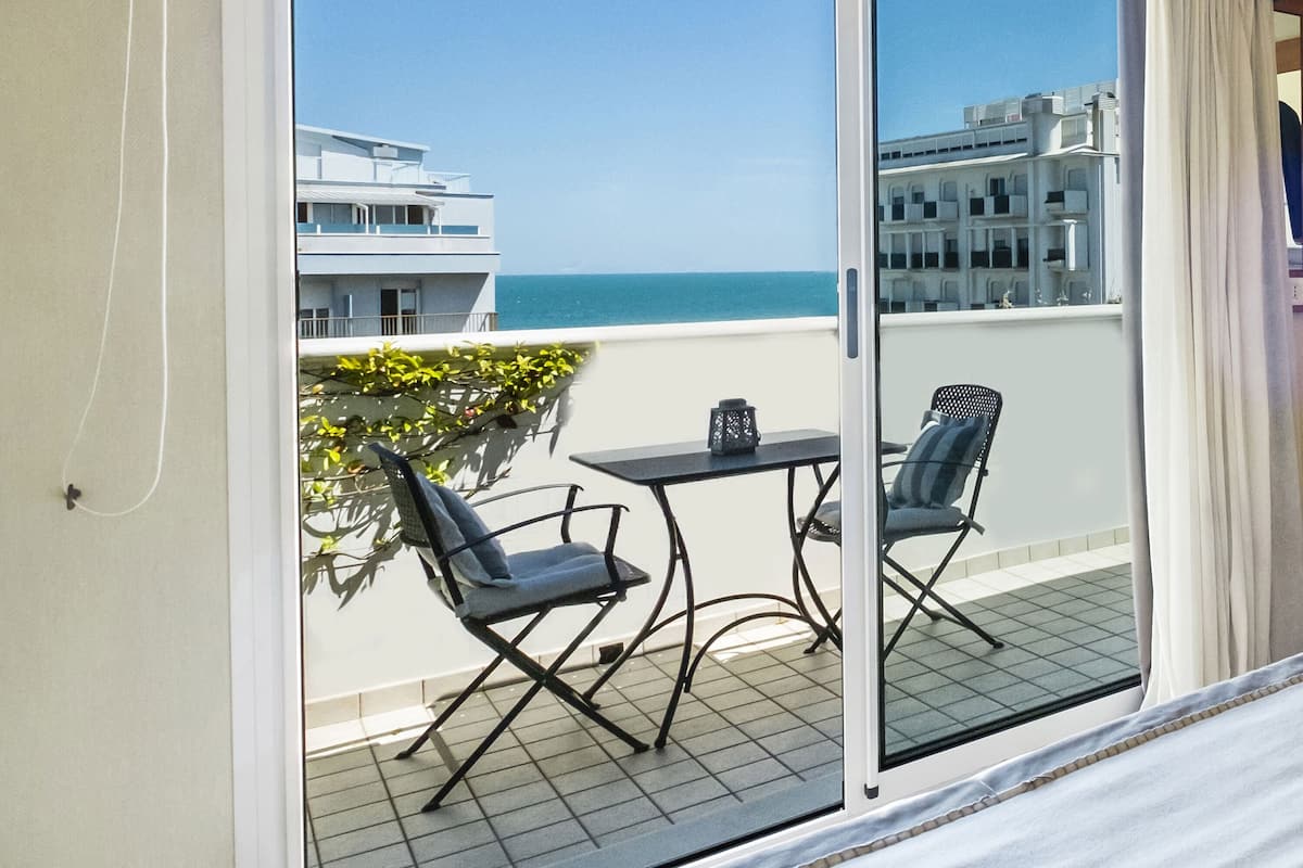 Un balcon avec une table et des chaises, d’où l’on peut admirer un immeuble et la mer.