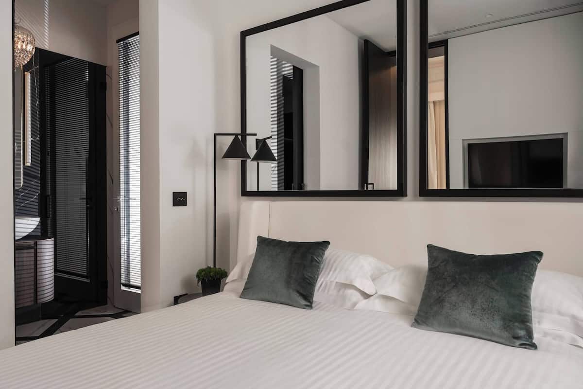 Une chambre d’hôtel moderne avec un grand lit, deux oreillers, une table de chevet, un miroir et un téléviseur.