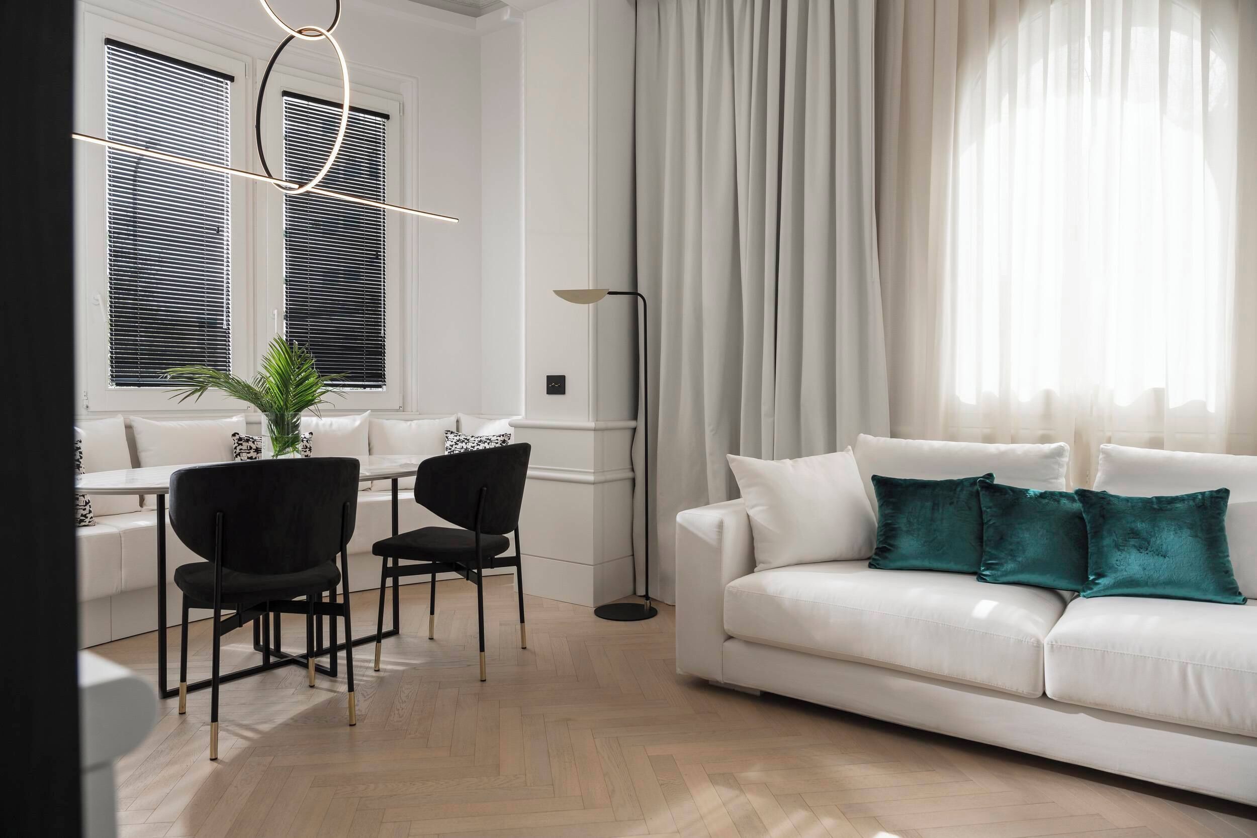A modern living room with a white sofa, black chairs, a dining table, and a floor lamp.