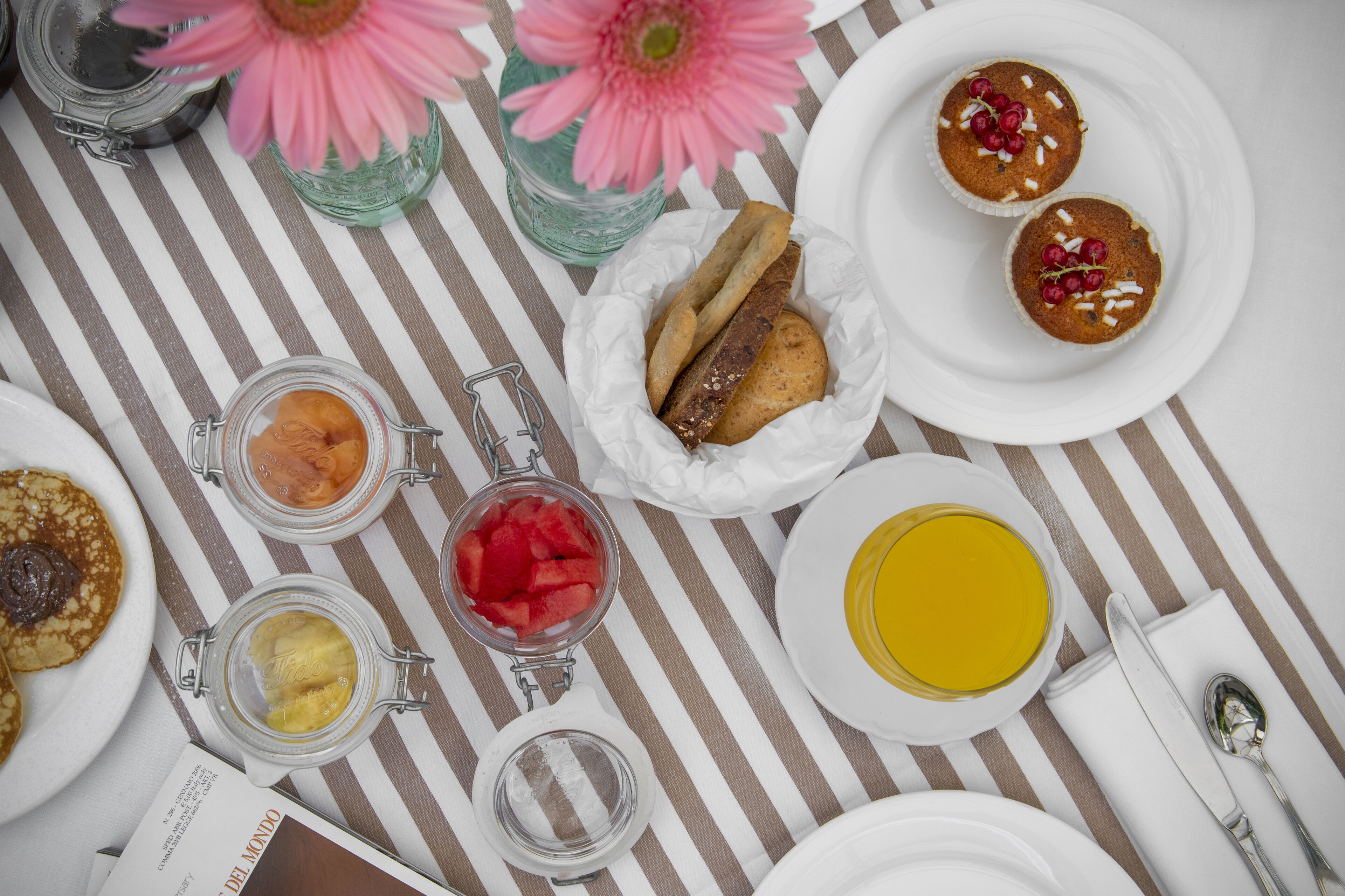 Una mesa con diferentes alimentos para desayuno, como panqueques, muffins y un vaso de jugo de naranja.
