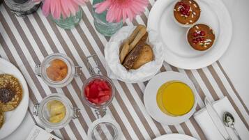Una mesa con diferentes alimentos para desayuno, como panqueques, muffins y un vaso de jugo de naranja.