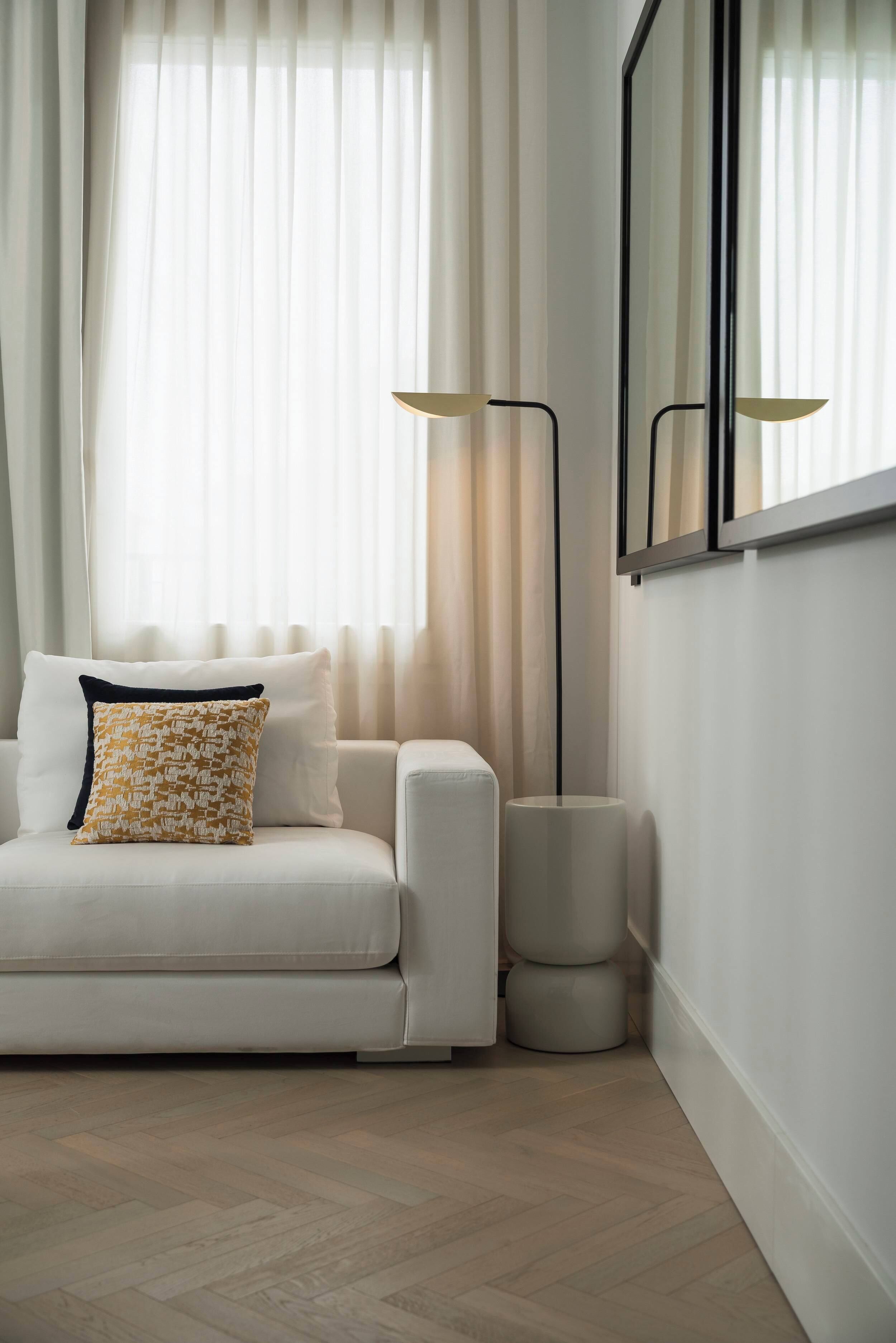 A modern living room with a white sofa, a patterned throw pillow, and a floor lamp.