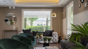 Een moderne woonkamer met een bank, fauteuils, een salontafel en een groot raam met uitzicht op groen.