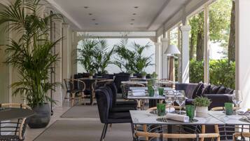 Un restaurante con terraza, mesas, sillas y plantas en macetas.
