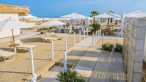 Een café aan het strand met terras, parasols en uitzicht op zee.