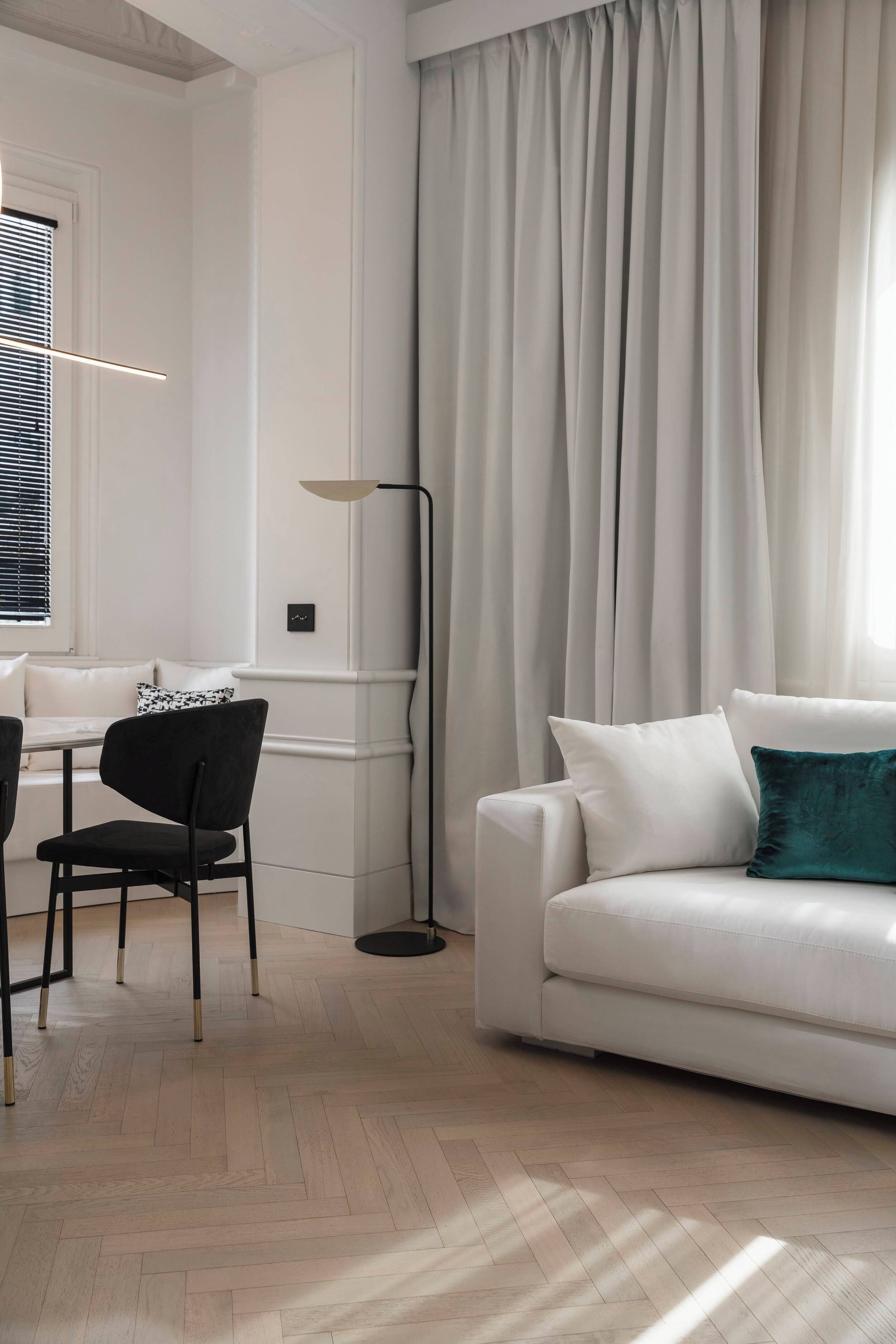 A modern living room with a white sofa, a black chair, a dining table with chairs, and a floor lamp.