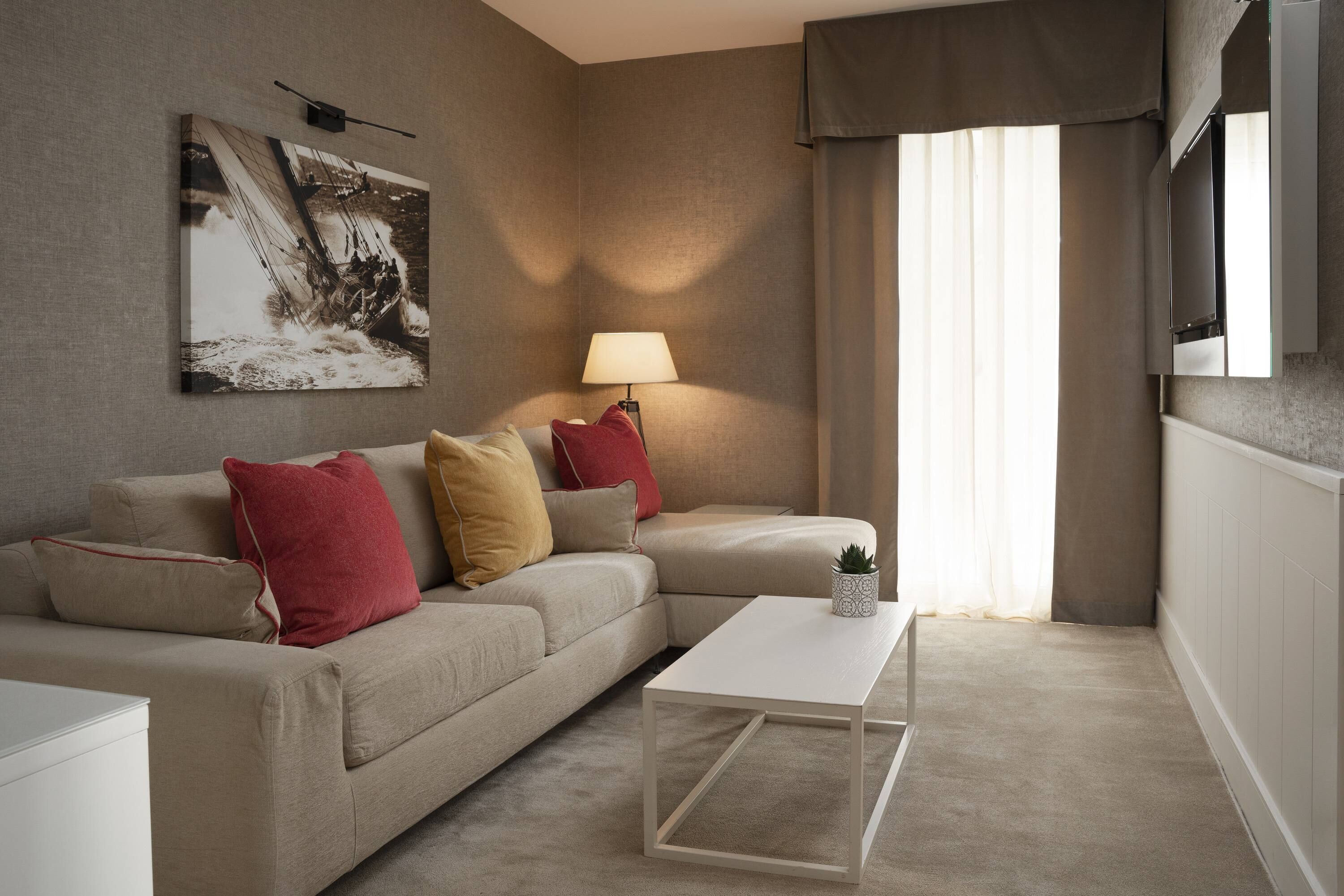 A modern living room with a beige sofa, a white coffee table, and a painting on the wall.