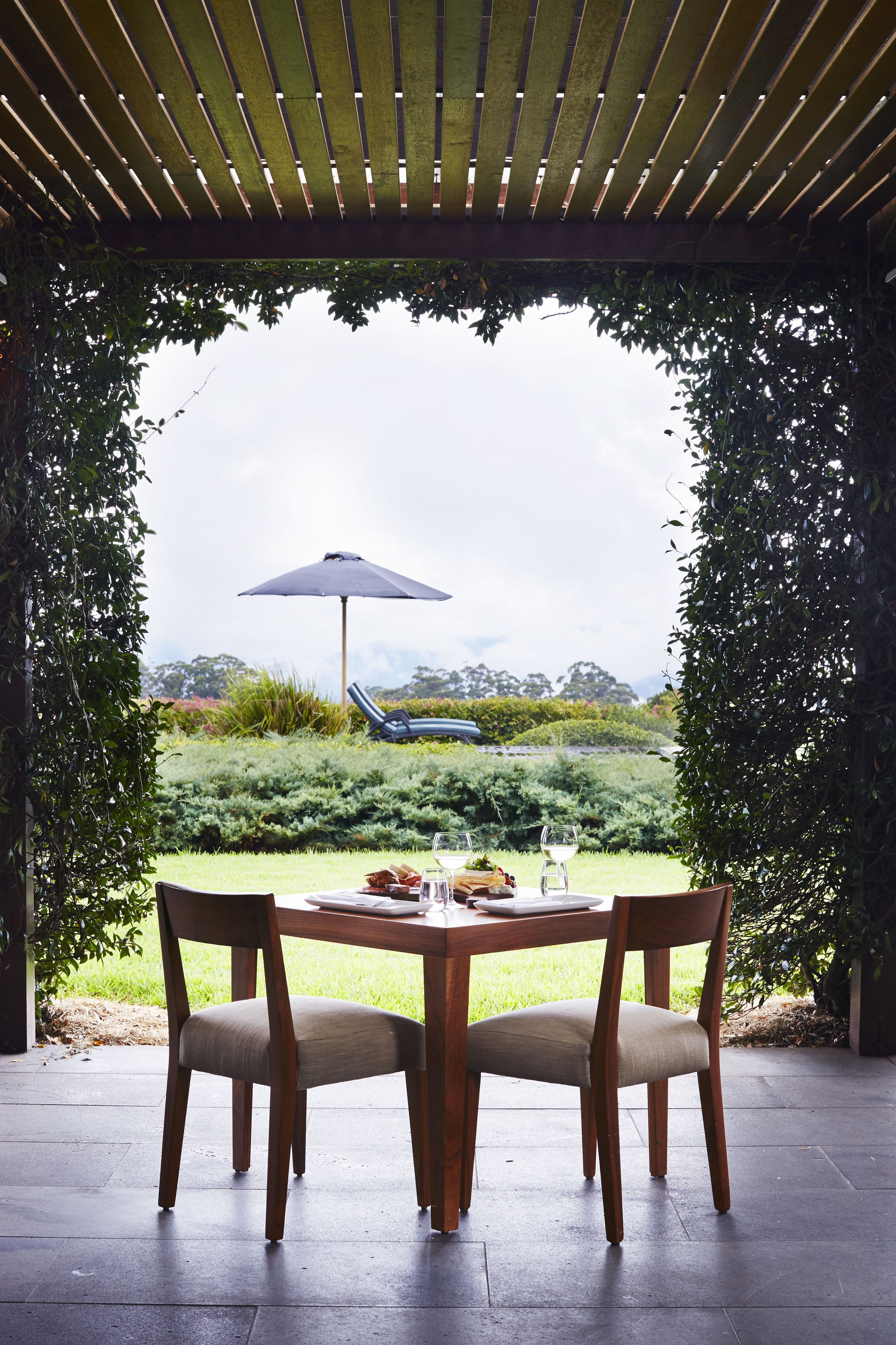 A covered outdoor dining area with a table and chairs, an umbrella, and a view of the landscape.