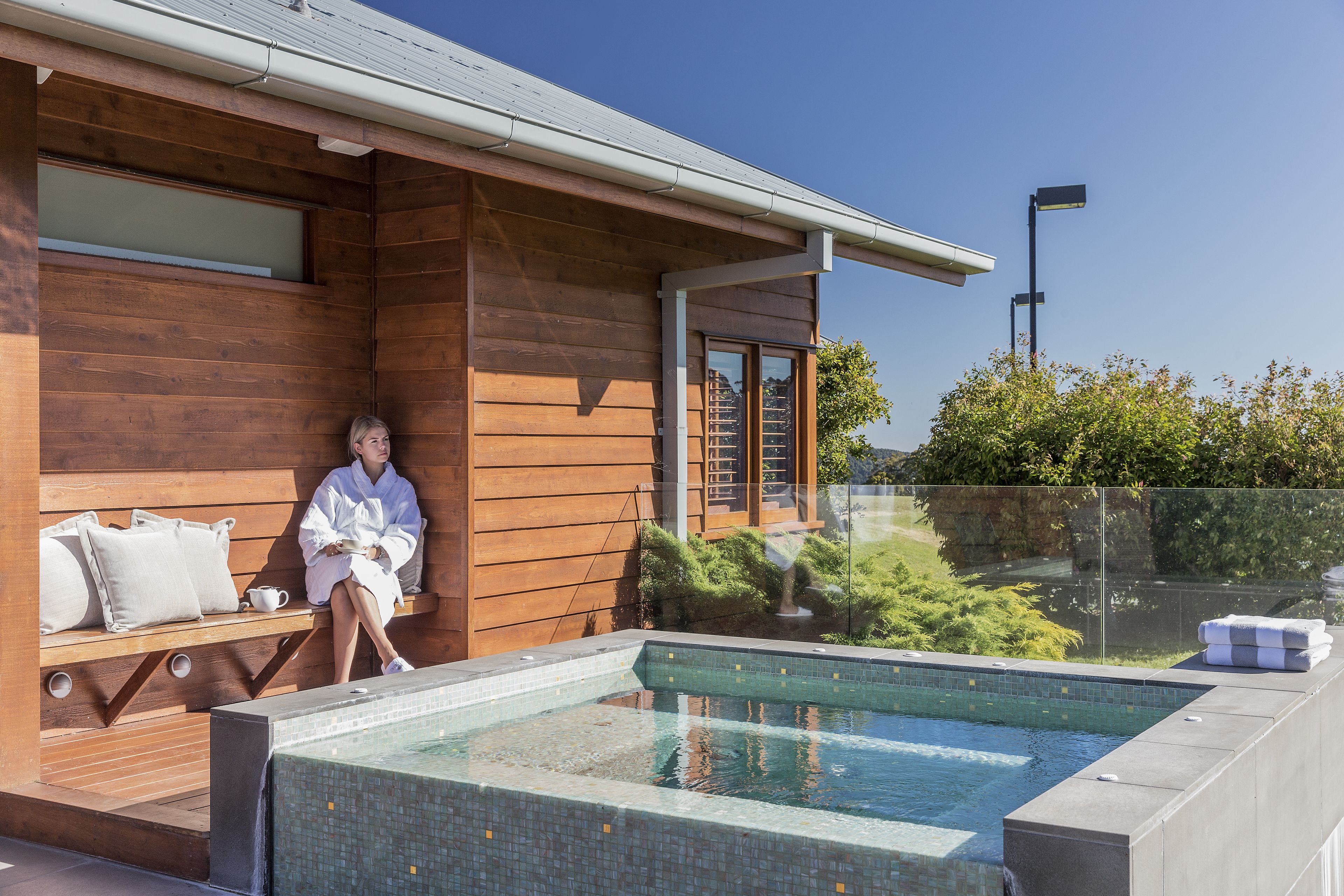 A wooden cabin with a swimming pool, a bench, and a glass railing.