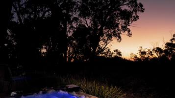 Ein Whirlpool mit blauer Beleuchtung, umgeben von Bäumen und einem Sonnenuntergang im Hintergrund.