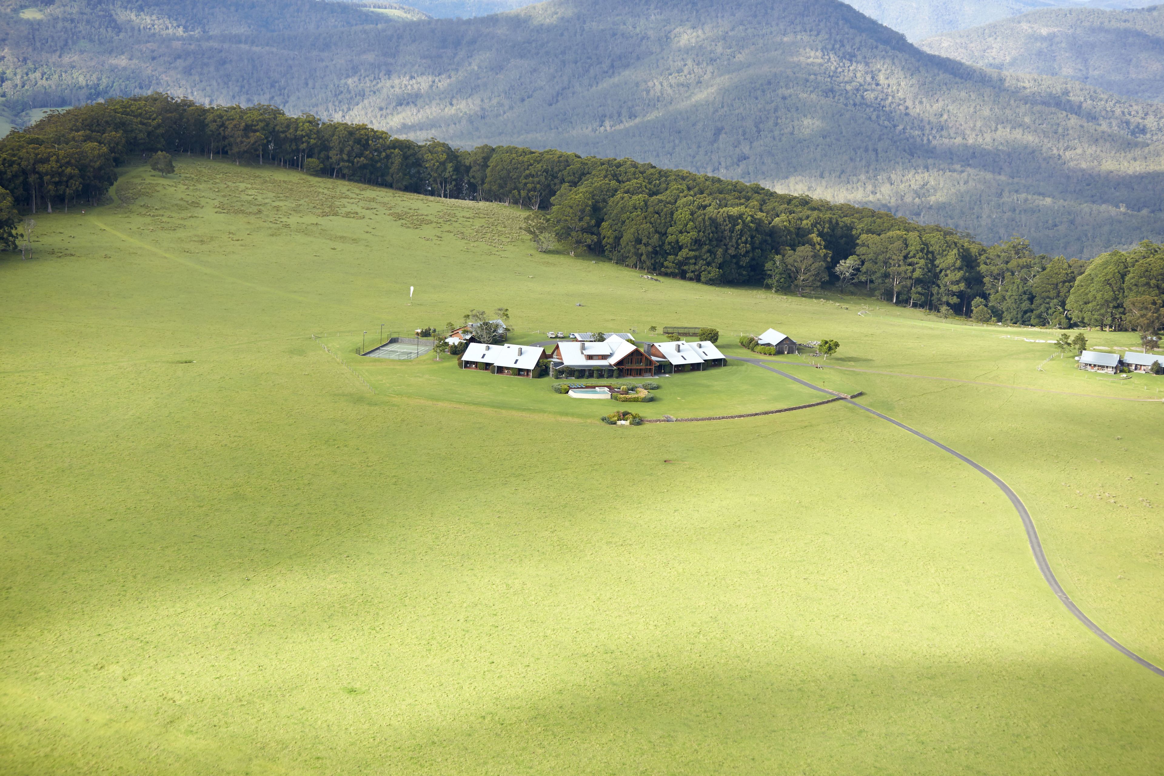 Un vaste champ ouvert, avec un ensemble de bâtiments, probablement une ferme ou un ranch, entouré de collines boisées.