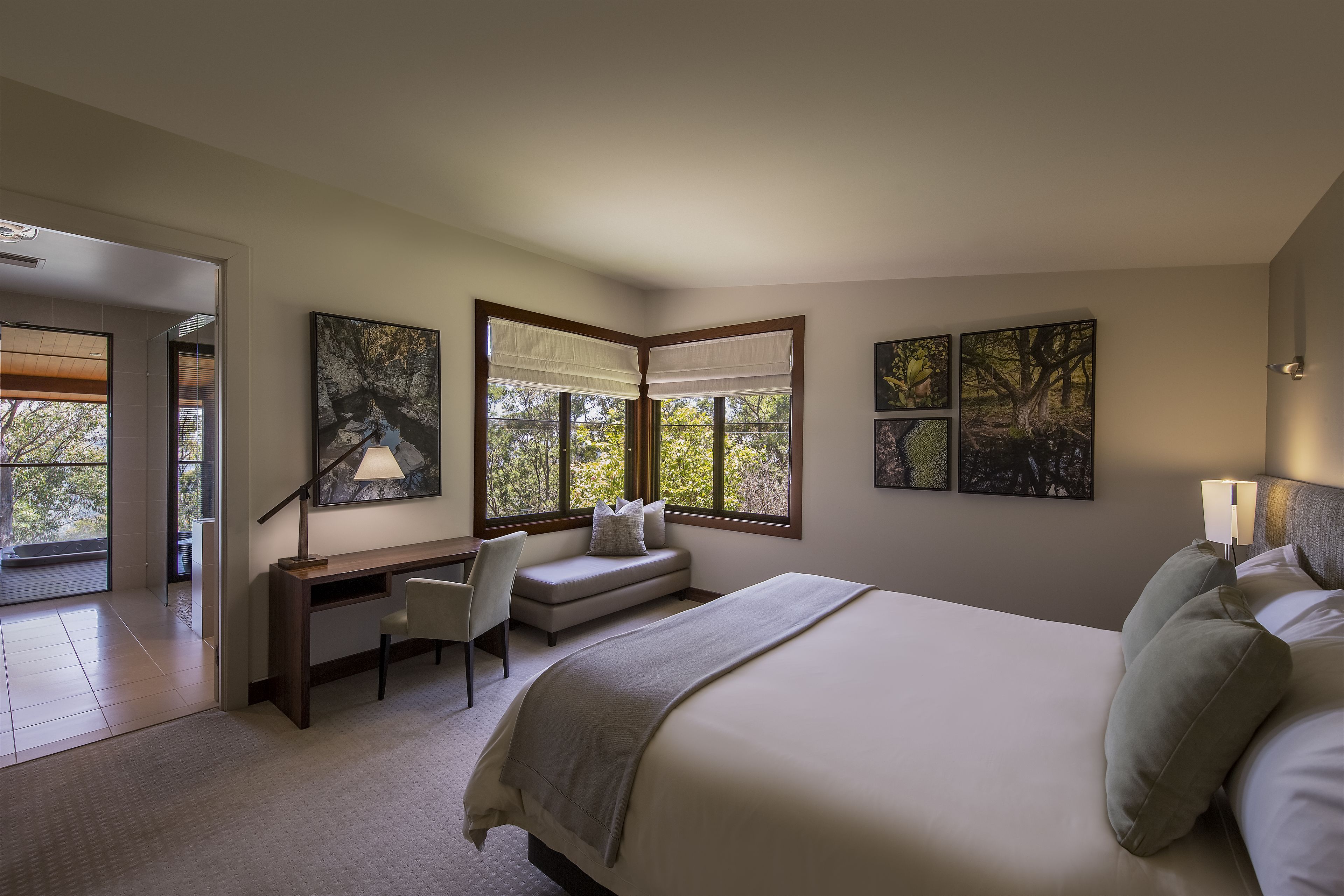 A modern bedroom with a large bed, a desk, and a window with a view of trees.
