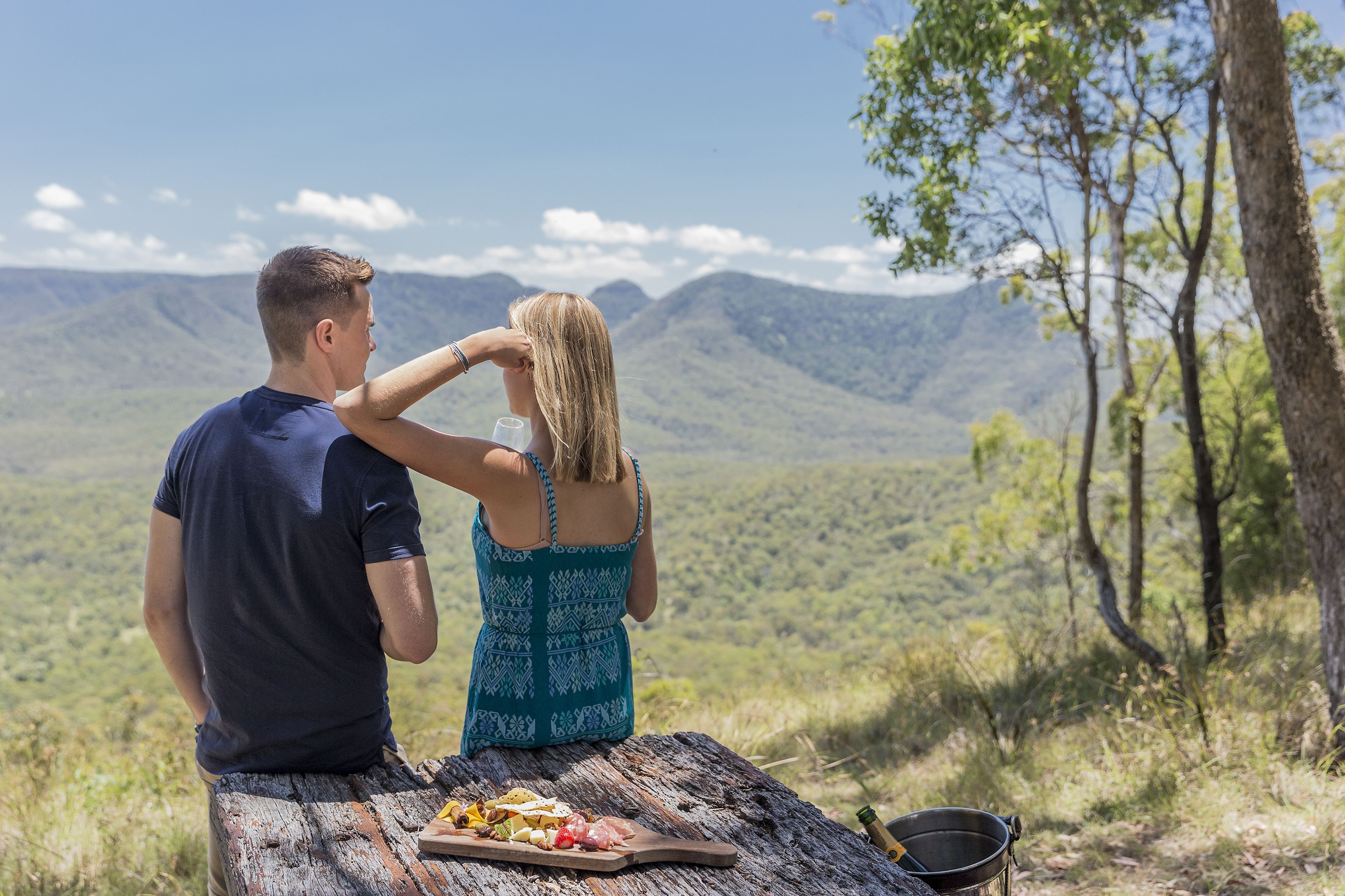 Un couple est assis sur un banc en bois, face à un paysage montagneux.