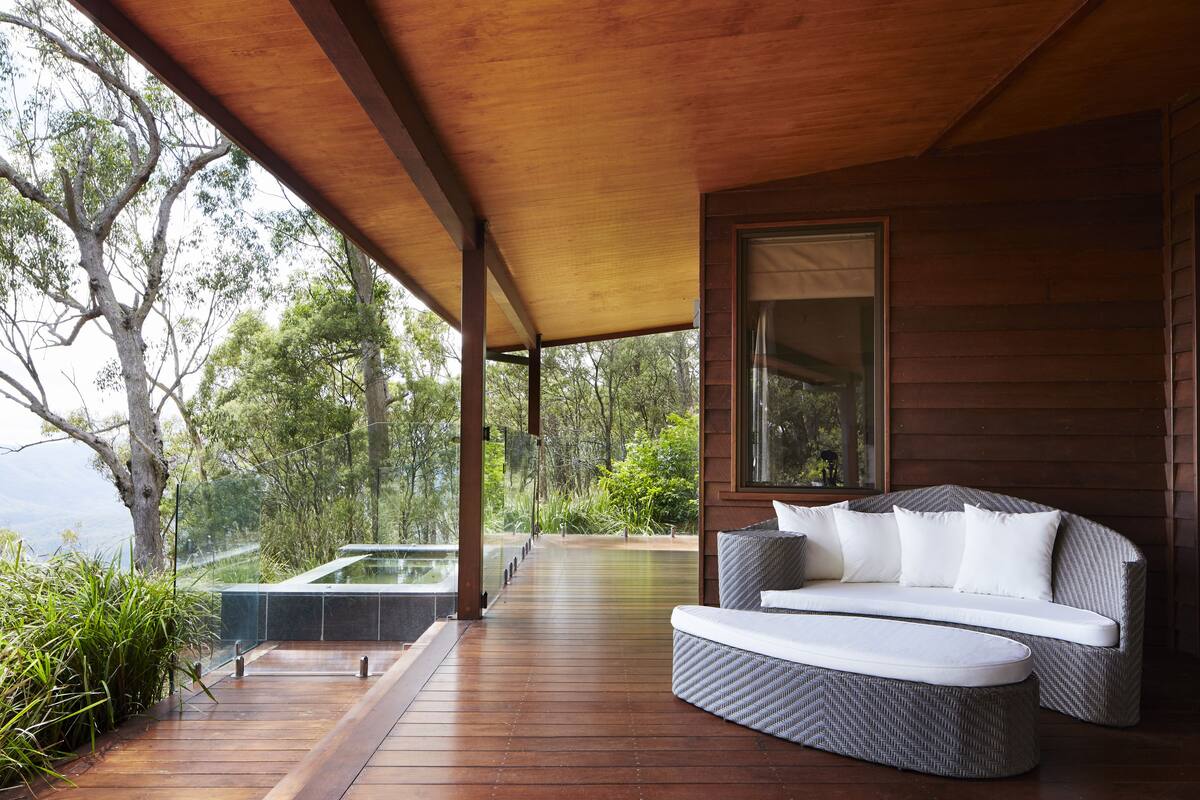 A wooden deck with a sofa and a glass-enclosed hot tub.